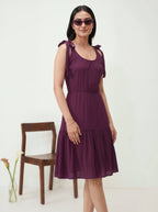 Woman wearing a purple dress standing next to a wooden chair on a white background