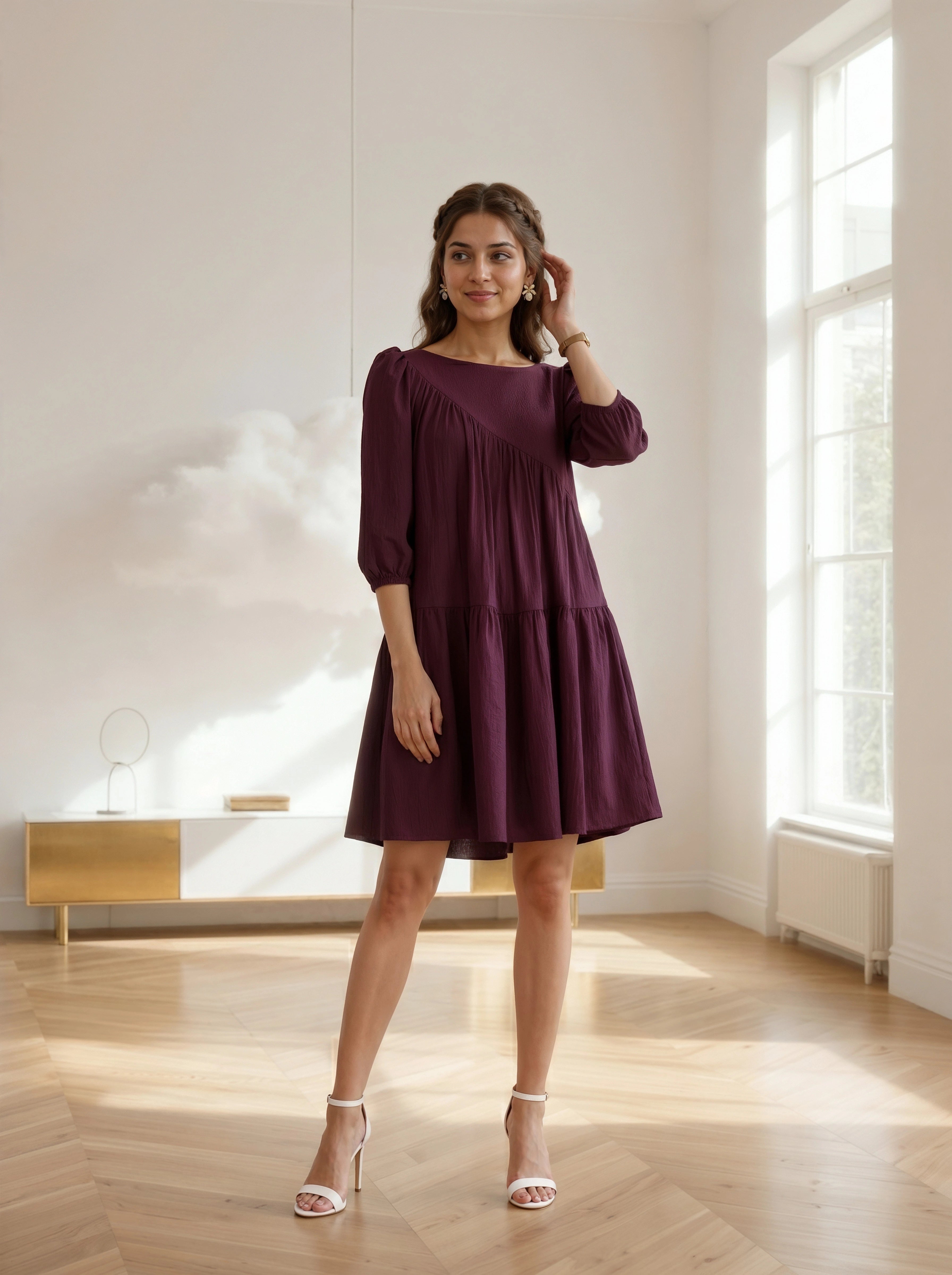Woman in a purple dress standing in a bright room with large windows.