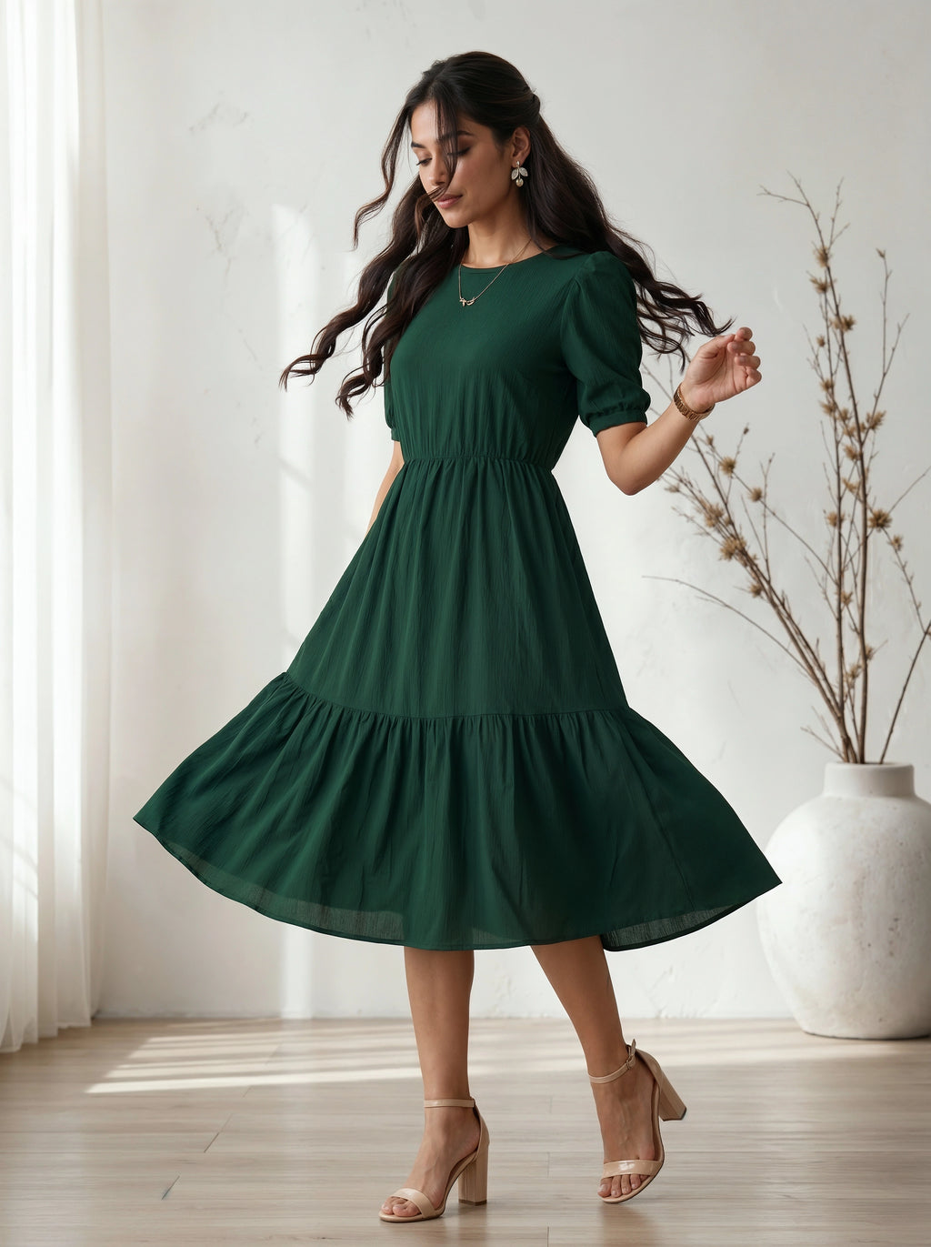 Woman wearing a green dress standing in a bright room with a vase in the background