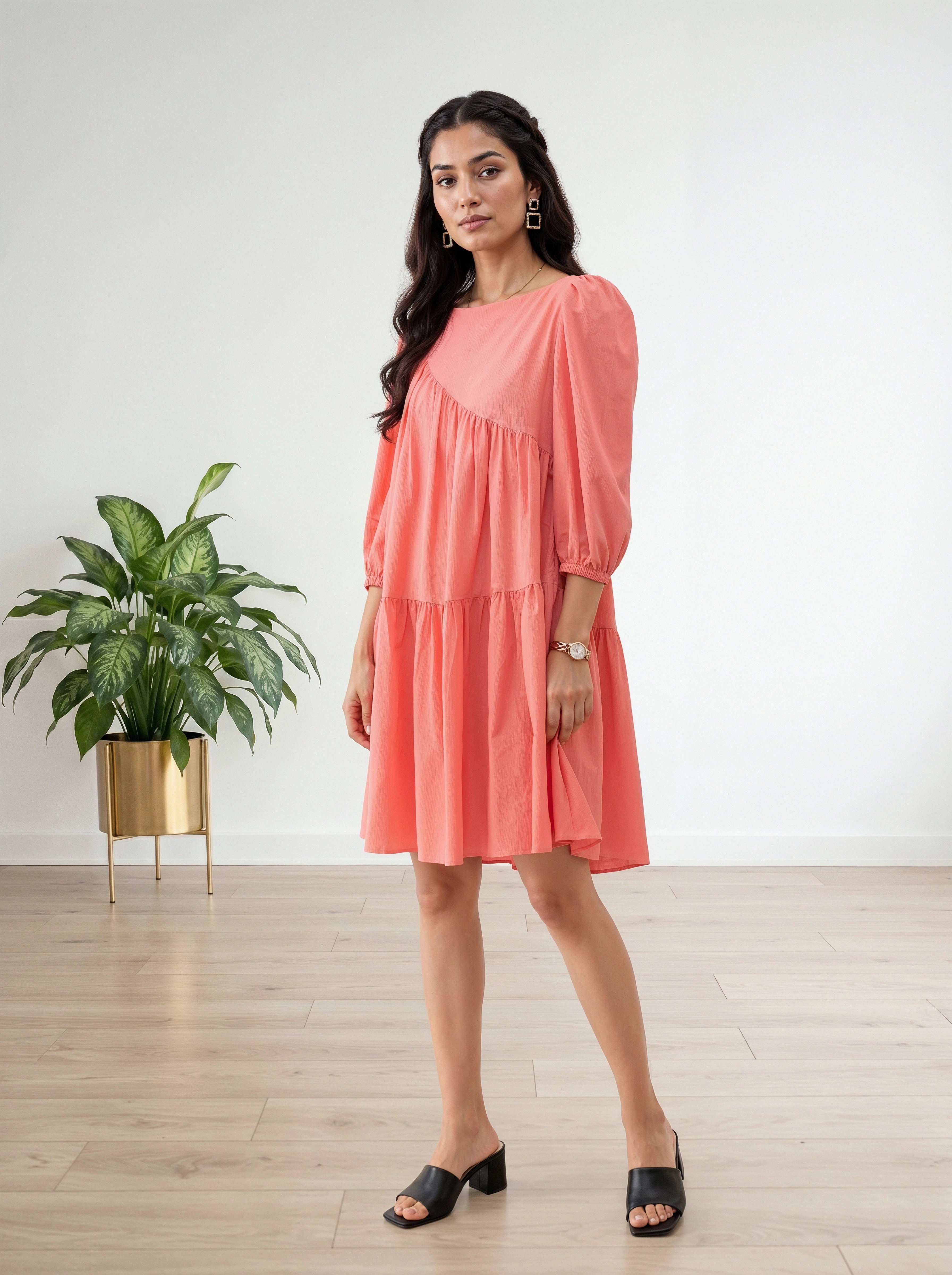 Woman wearing a coral dress standing in a minimalistic room with a plant.