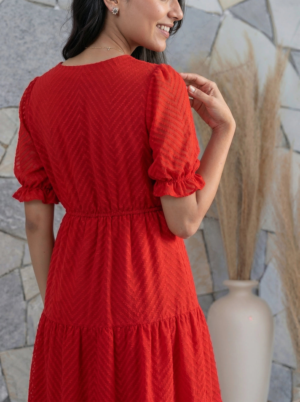 Woman wearing a red dress with a textured pattern, standing against a stone wall.