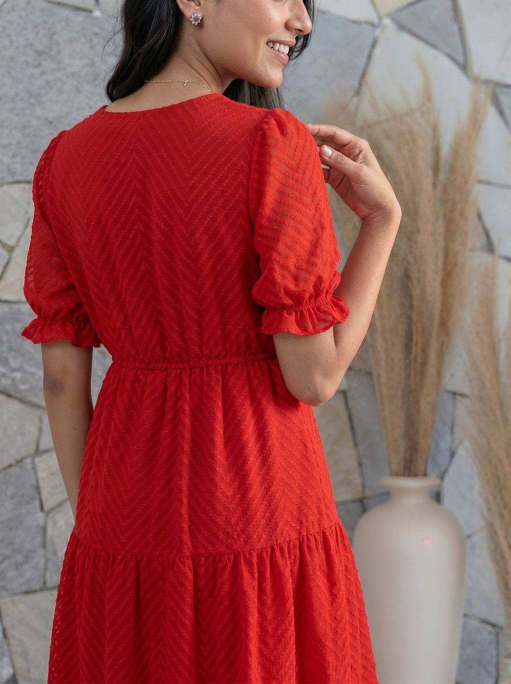 Woman wearing a red dress with a textured pattern, standing against a stone wall.