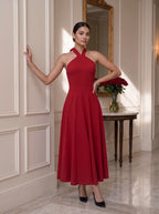 A woman viewed from behind wearing a sage green tiered dress with puff sleeves and a keyhole back detail, styled with a white bow in her hair in a warm, decorated indoor setting.