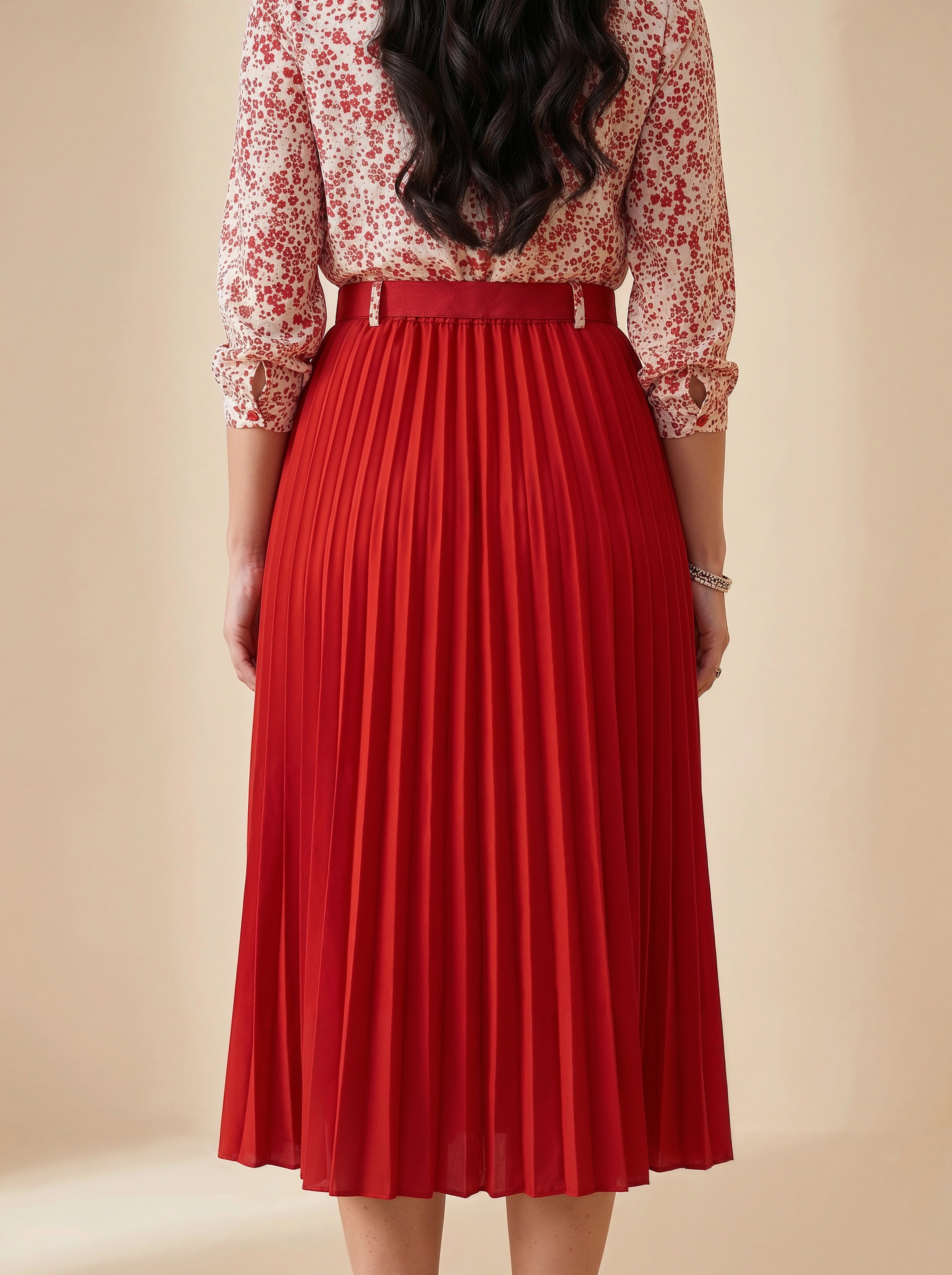 Person wearing a red pleated skirt with a floral blouse on a beige background