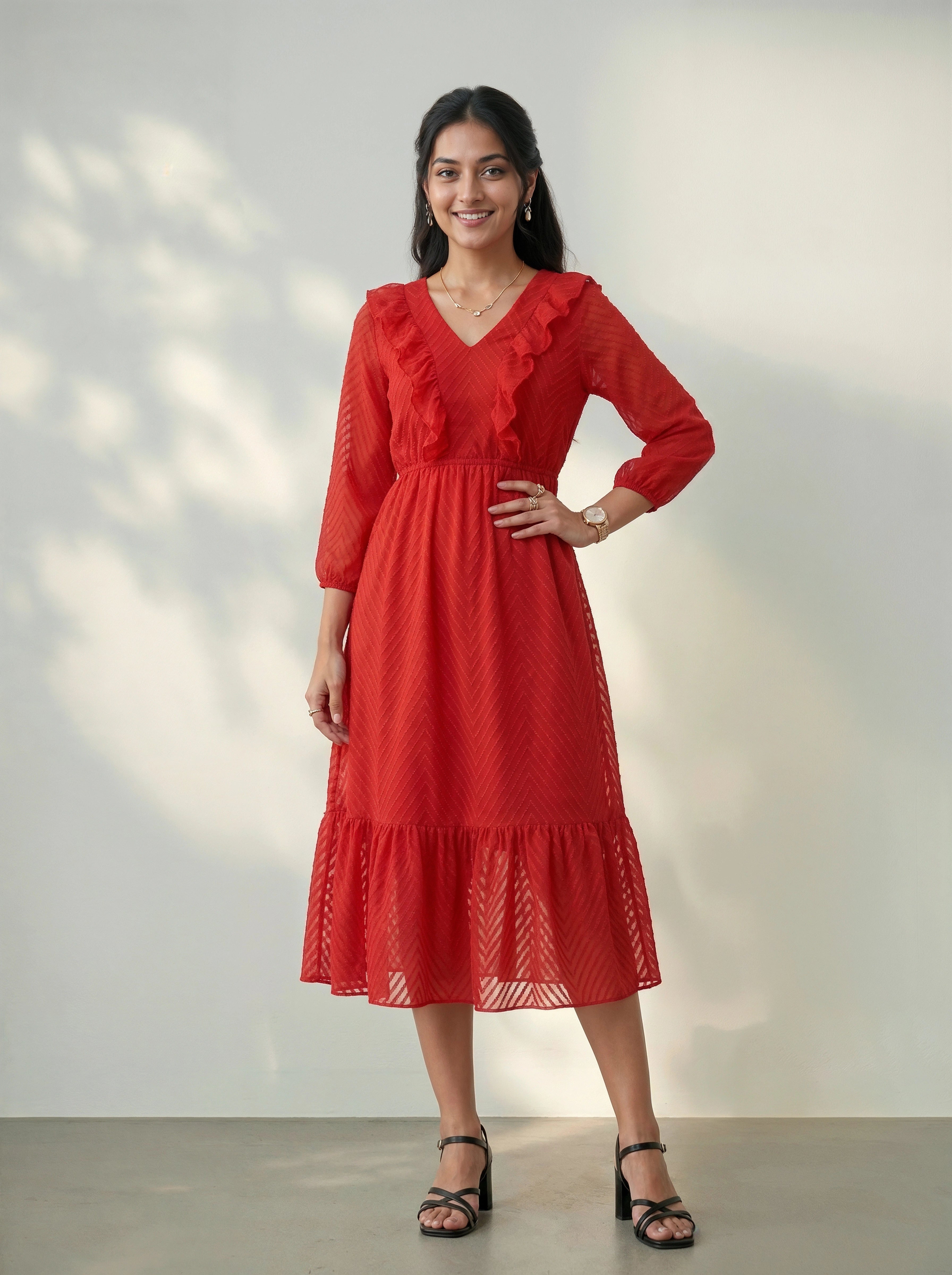 Woman wearing a red dress with ruffled sleeves and bottom hem against a white wall.