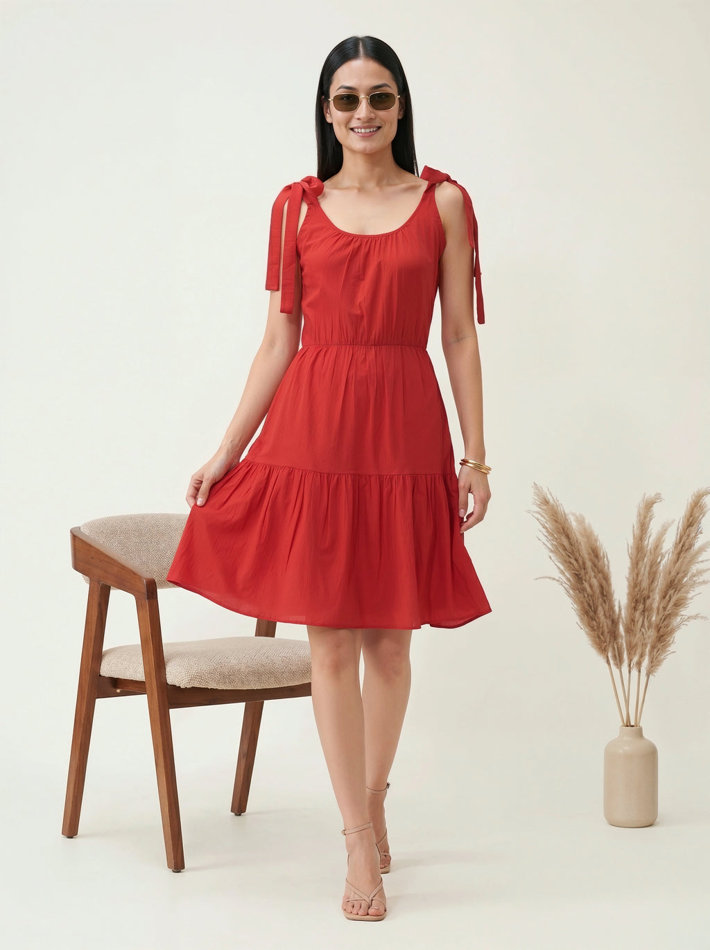 Woman wearing a red dress with bow straps in a minimalistic setting.