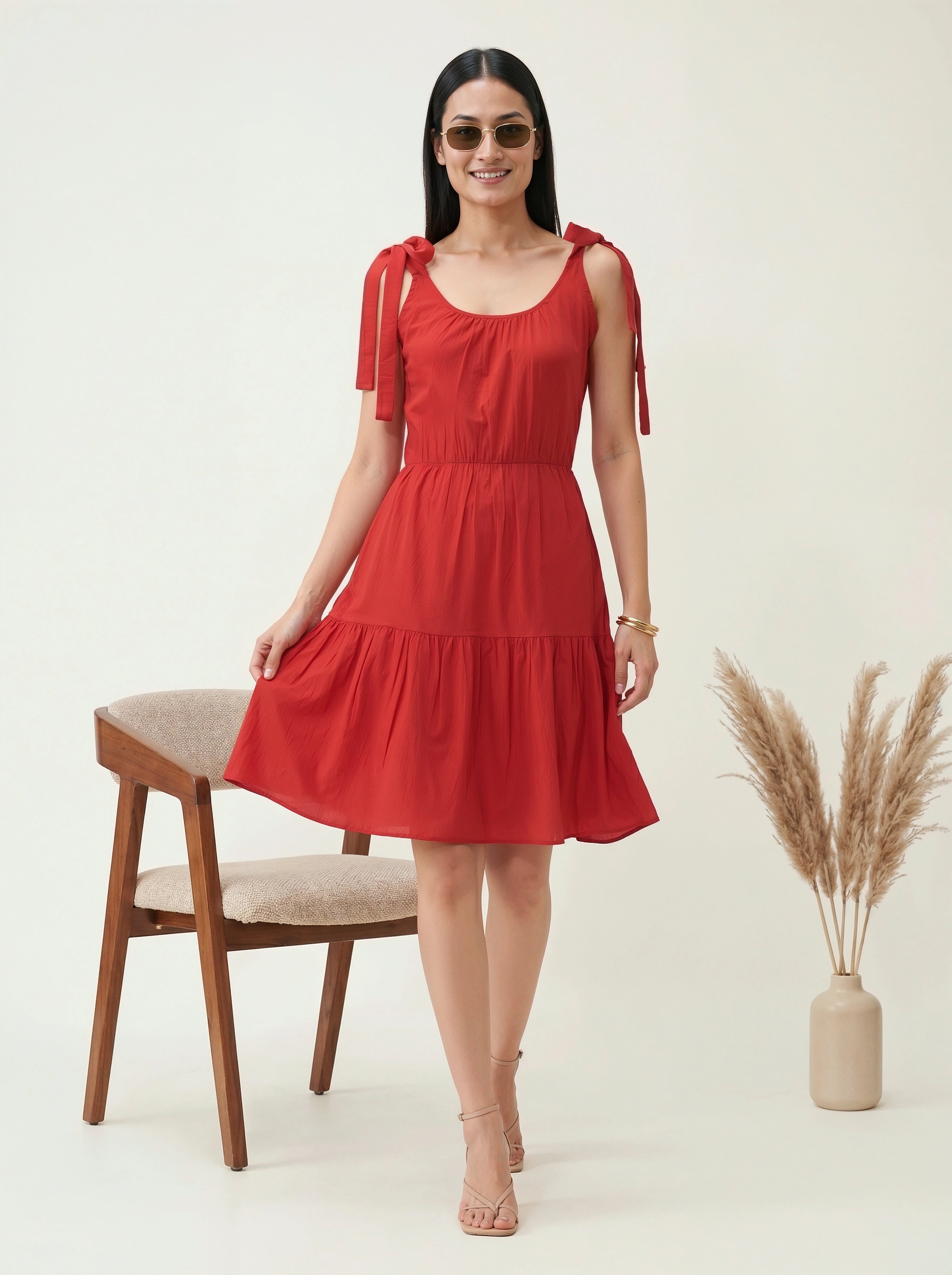 Woman wearing a red dress with bow straps in a minimalistic setting.