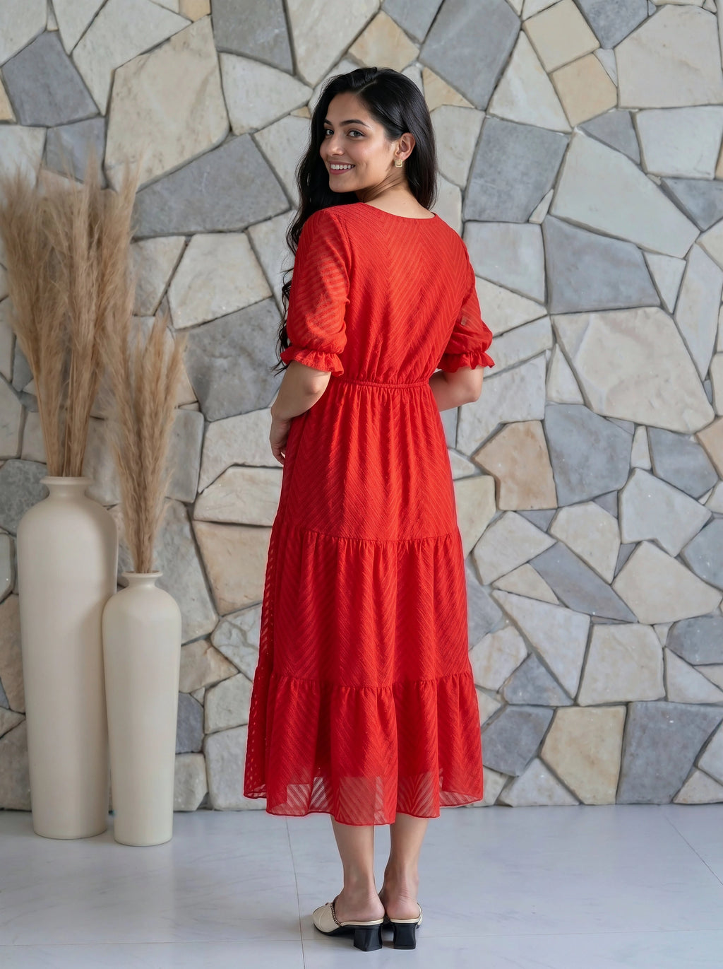 Woman in a red dress standing against a stone wall with decorative vases.