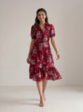 A woman modeling a three-quarter sleeve tiered midi dress in deep burgundy with sheer mesh side panels, paired with black ankle-strap heels, against a plain white studio background.