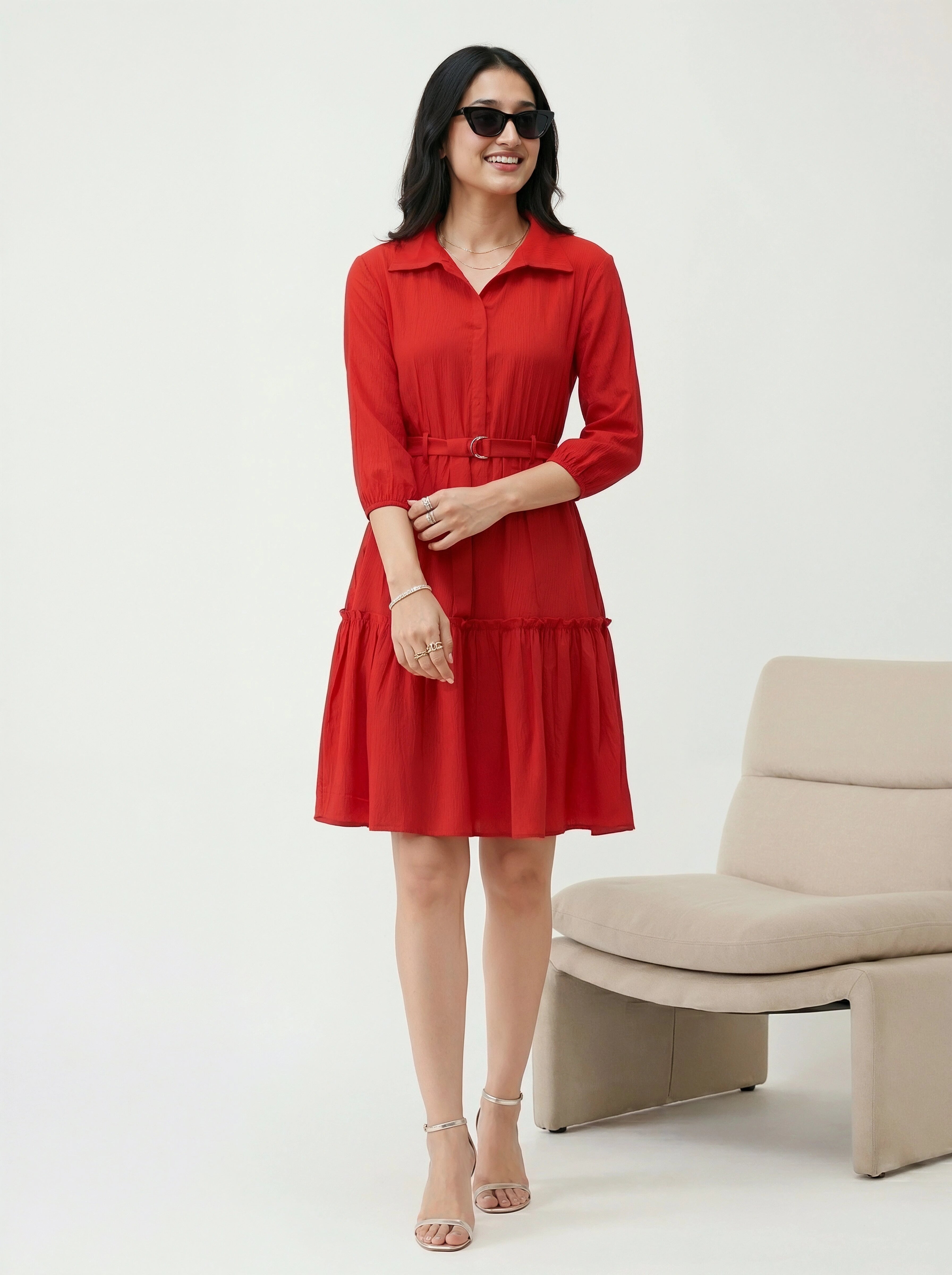 Woman wearing a red dress standing in a minimalistic room with a beige chair.