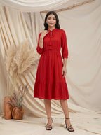 Woman wearing a red dress standing against a beige curtain with decorative plants.