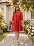 Woman in a red dress standing on a stone path with flowers and a house in the background