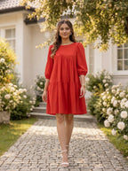 Woman in a red dress standing on a stone path with flowers and a house in the background