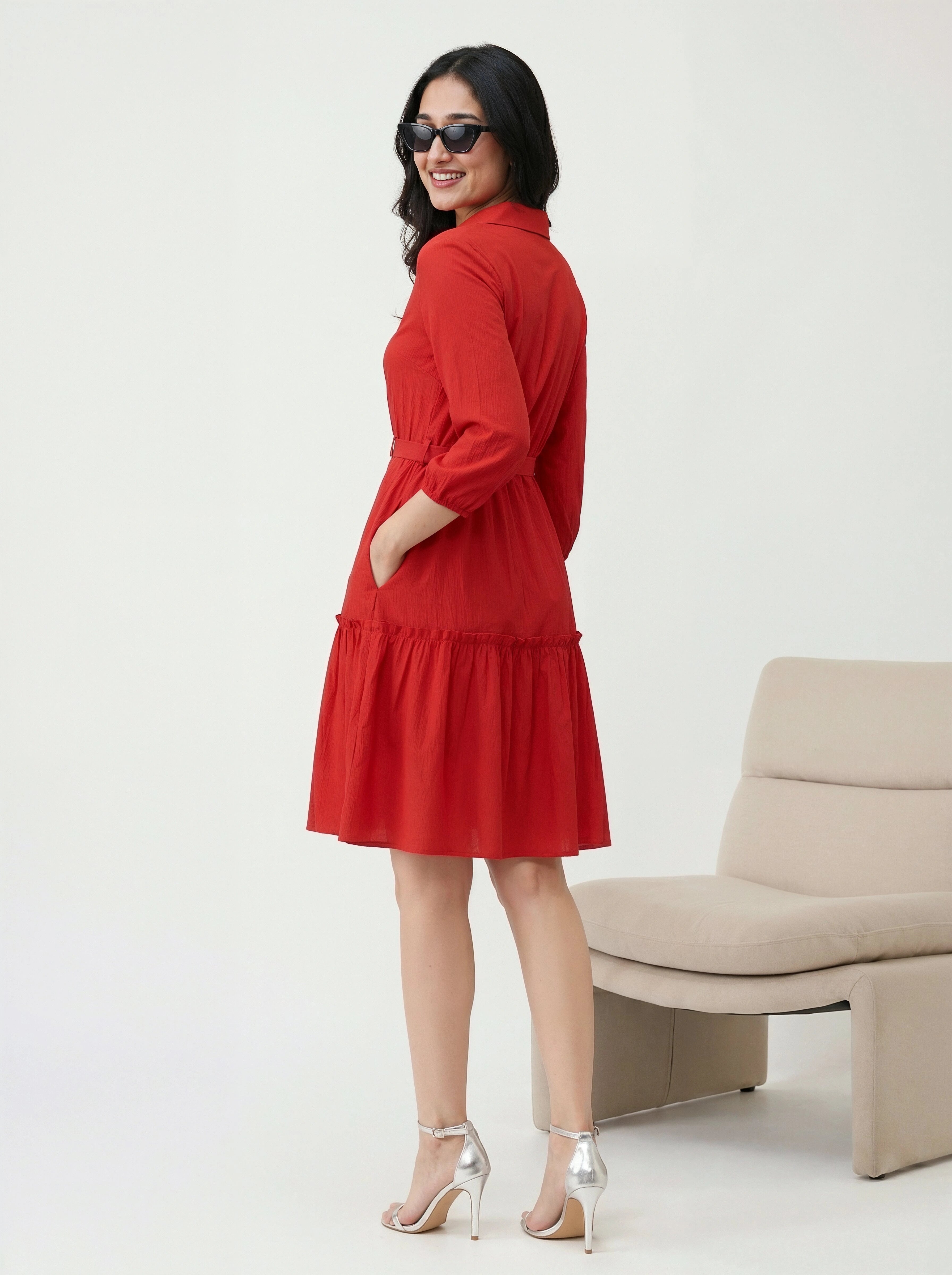 Woman wearing a red dress standing in a minimalistic room with a beige chair.