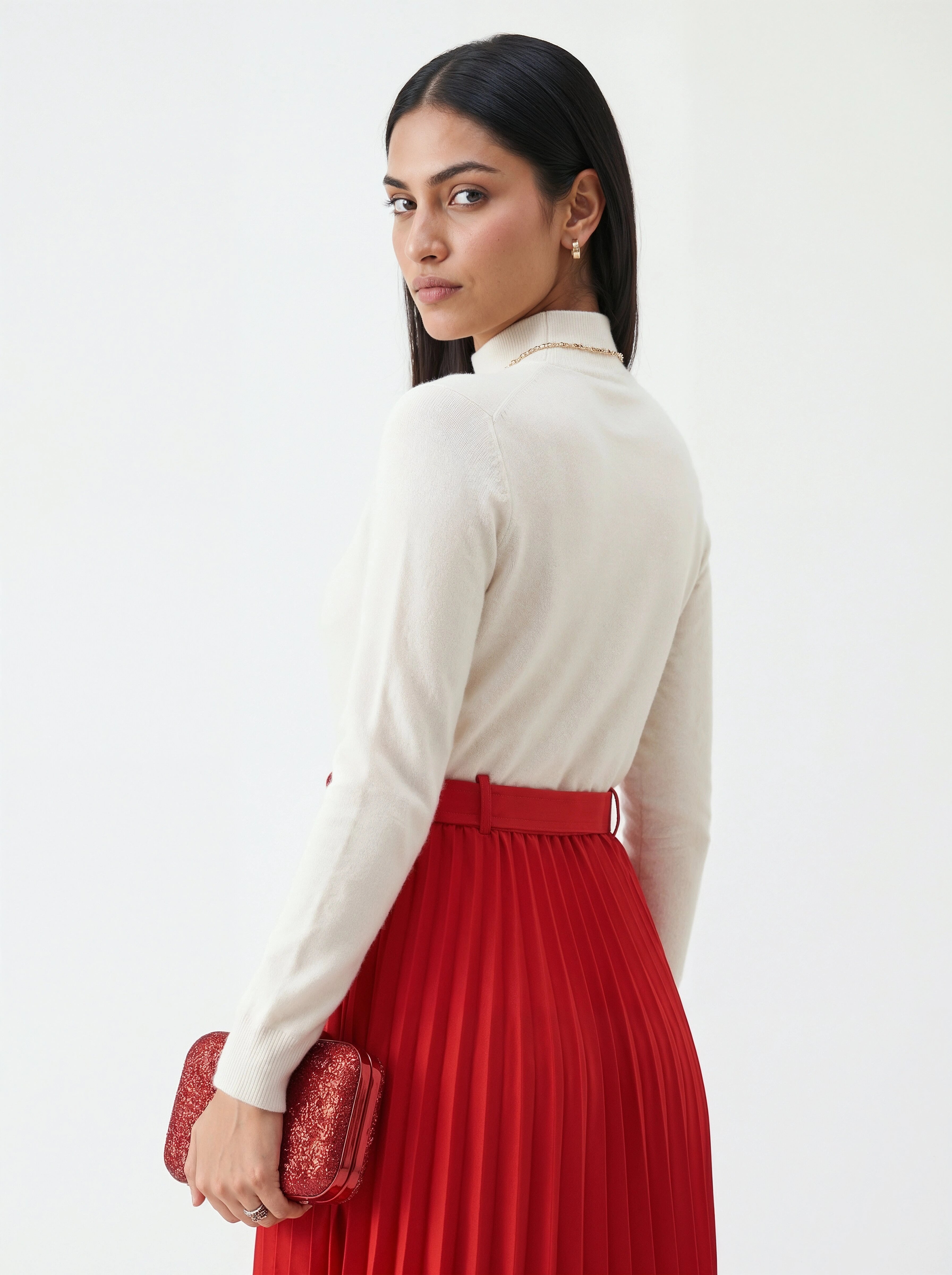 Woman wearing a white blouse and red pleated skirt holding a red clutch against a white background