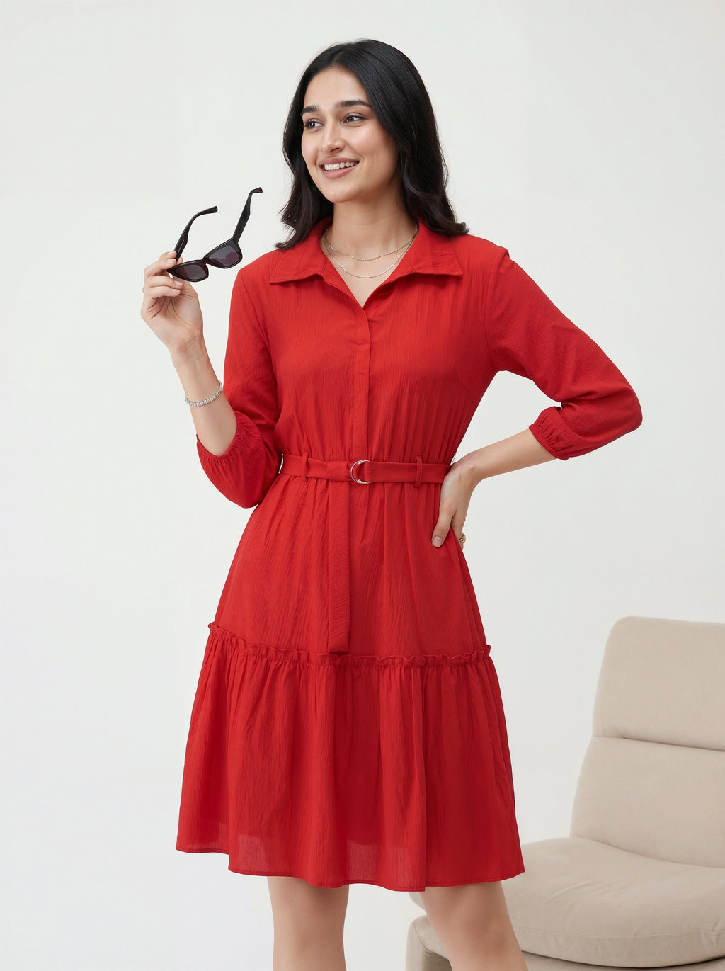 Woman in a red dress holding sunglasses against a white background