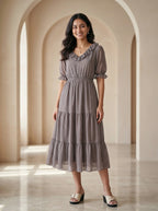 Woman wearing a gray dress standing in a sunlit room with arches.