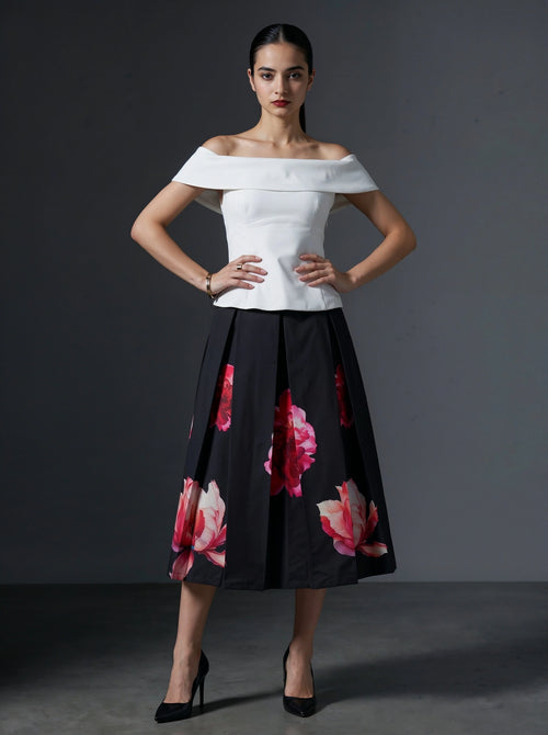 Woman wearing a white off-shoulder top and black floral skirt against a gray background