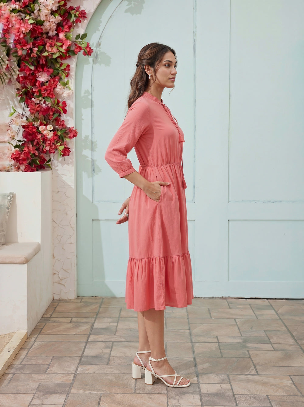 Woman in a pink dress standing in front of a floral wall and light blue door.