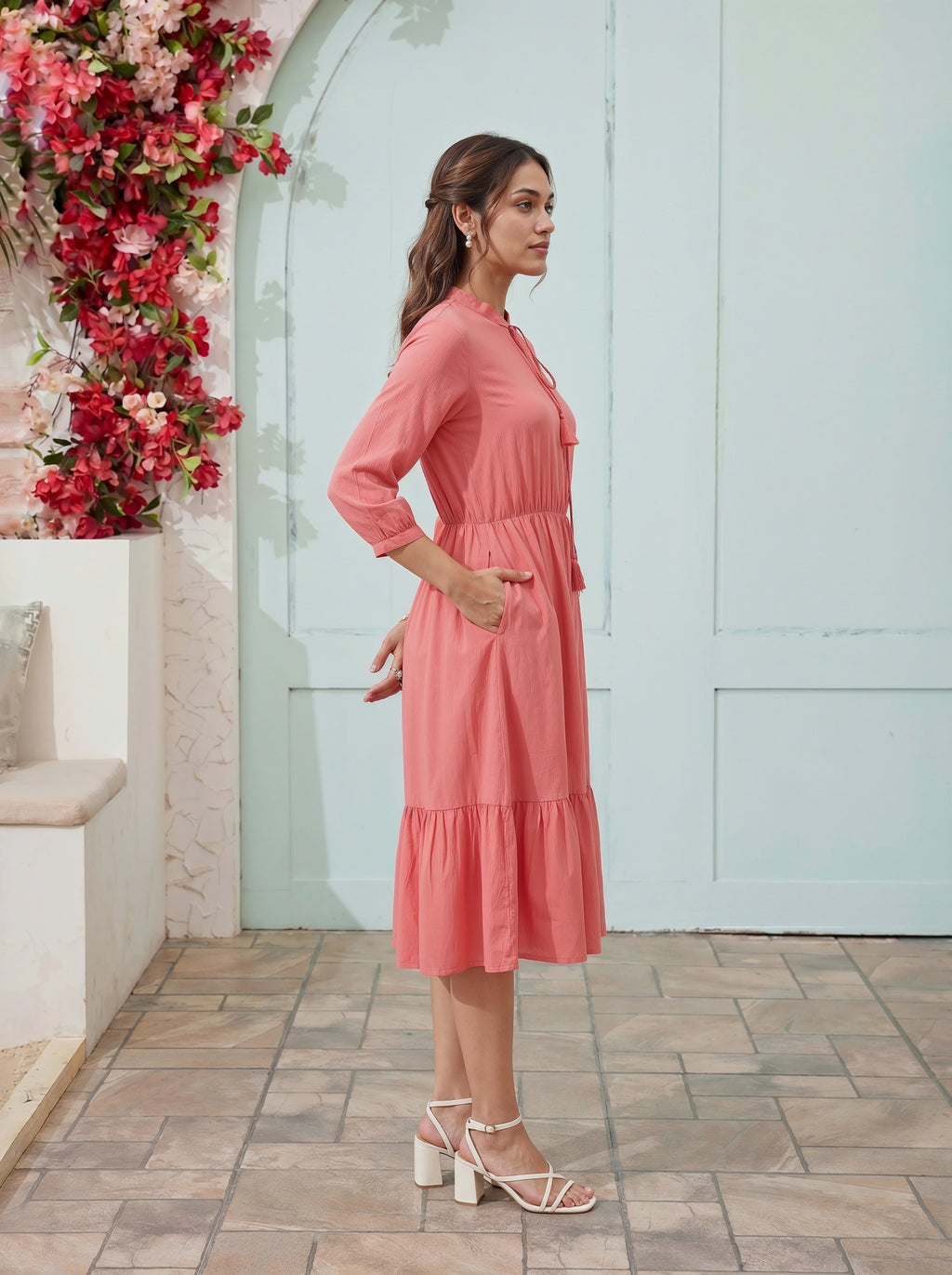 Woman in a pink dress standing in front of a floral wall and light blue door.