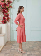 Woman in a pink dress standing in front of a floral wall and light blue door.