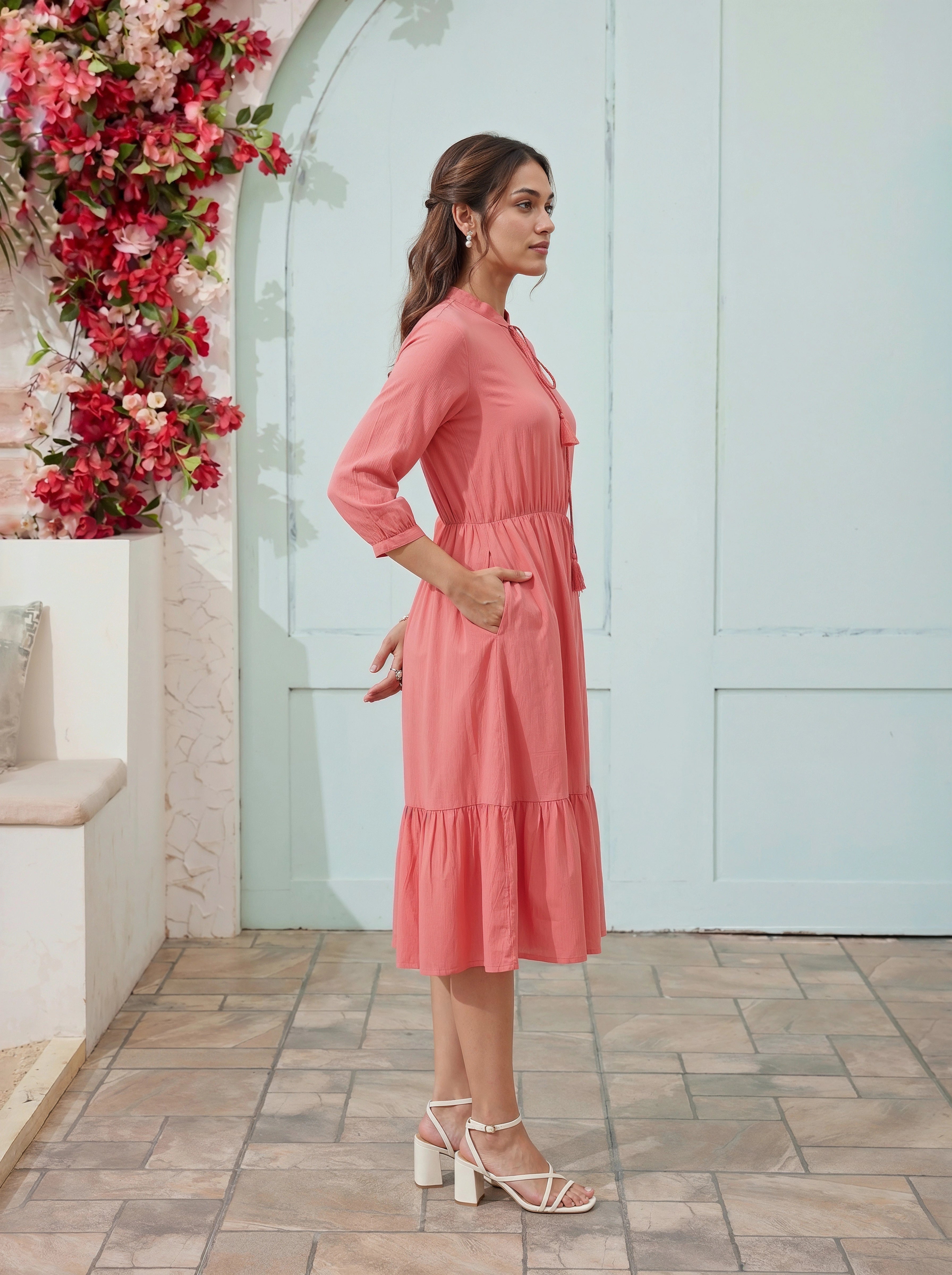 Woman in a pink dress standing in front of a floral wall and light blue door.