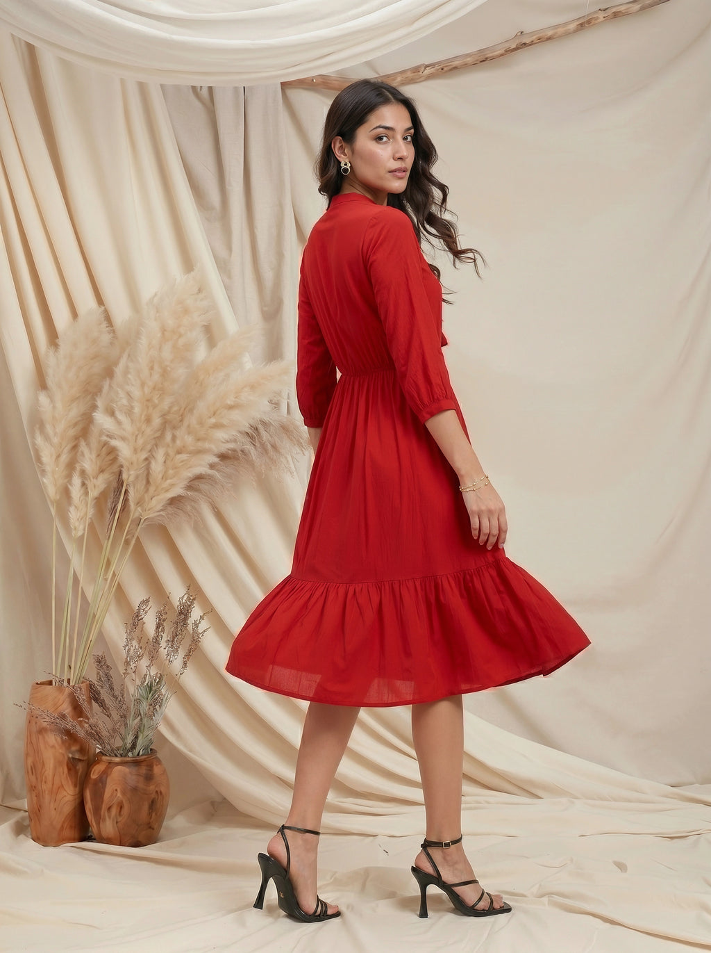 Woman in a red dress standing against a beige curtain with decorative elements.
