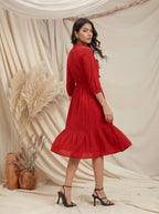 Woman in a red dress standing against a beige curtain with decorative elements.