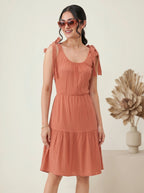 Woman wearing a terracotta dress with bow straps against a neutral background