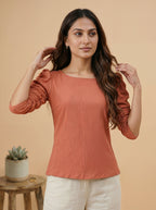 Woman wearing a rust-colored top with white pants against a beige background