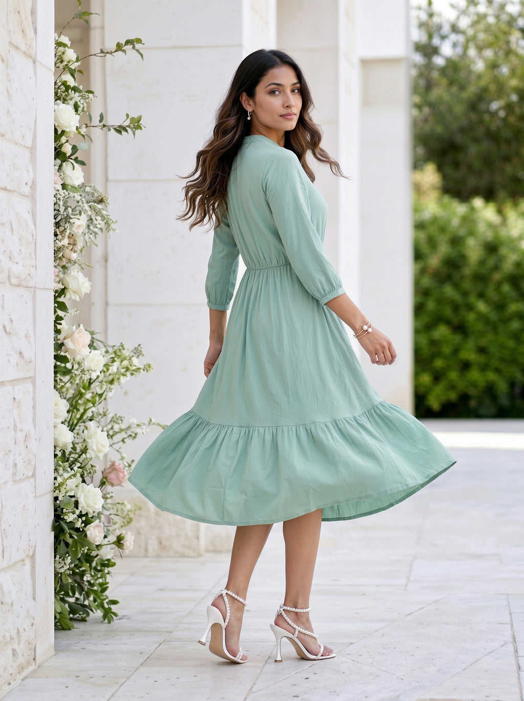 Woman in a light green dress standing outdoors near a white building with floral decorations.