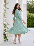 Woman in a light green dress standing outdoors near a white building with floral decorations.