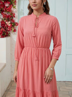 Woman wearing a pink dress standing in front of a white wall with floral decorations.