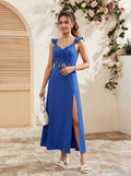 A woman models a royal blue sleeveless maxi dress with ruffled shoulder straps, a gathered sweetheart neckline, a side cutout, and a high thigh slit. She is standing in a sunlit courtyard with a beige stucco wall, floral arch, and tiled floor.