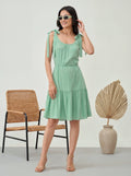 Woman in a light green dress standing next to a wicker chair and decorative vase.
