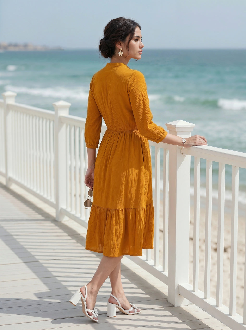 Woman in a yellow dress standing on a wooden deck by the ocean.