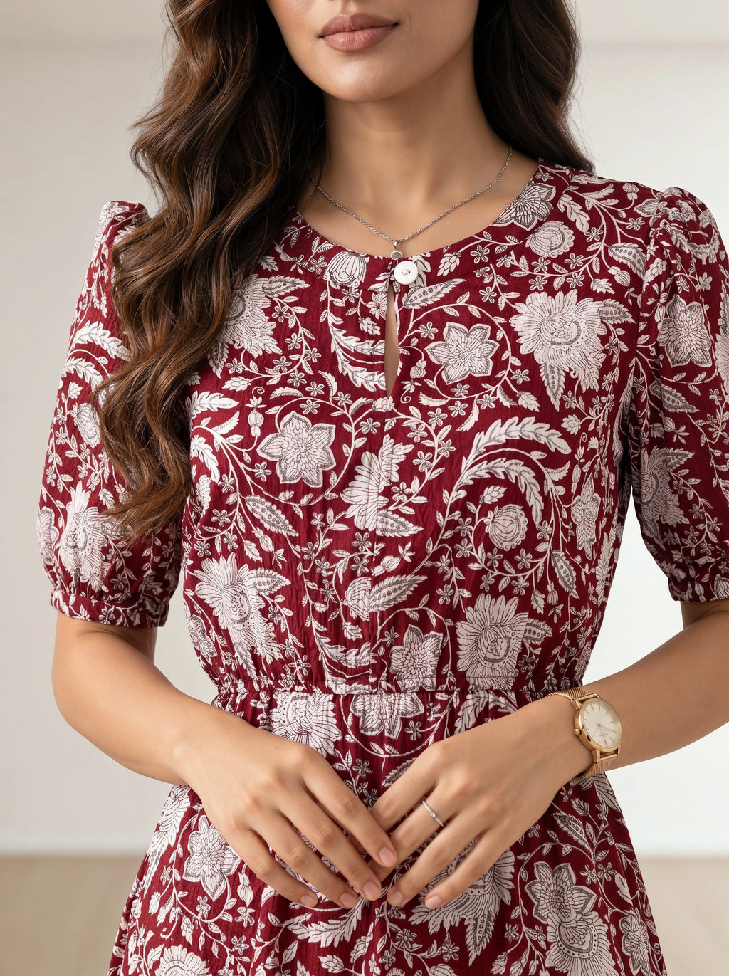 A woman wearing a short-sleeve red dress with a white floral toile pattern, featuring puff sleeves, a round neckline with a decorative keyhole button closure, and a gathered waist.