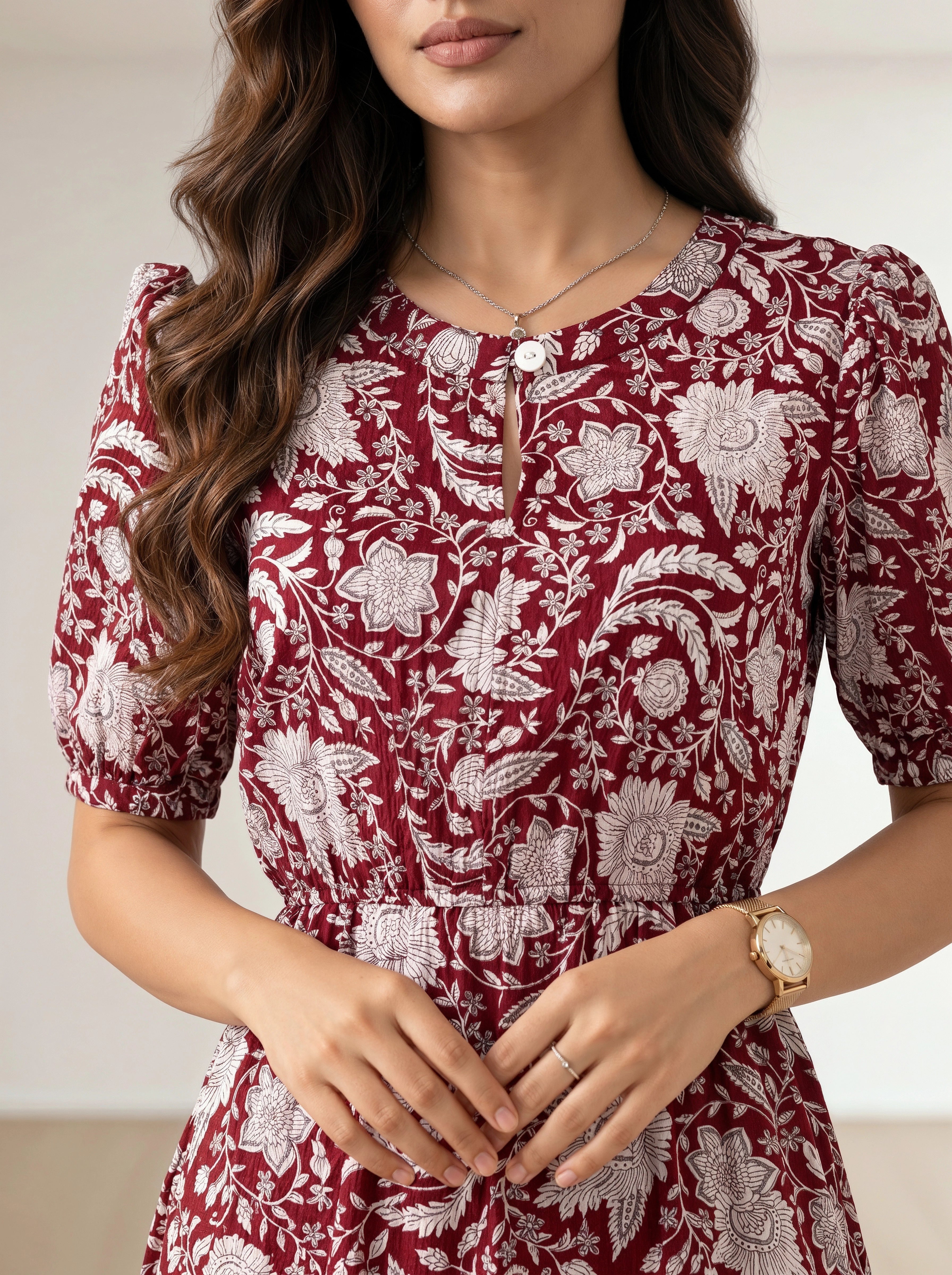 A woman wearing a short-sleeve red dress with a white floral toile pattern, featuring puff sleeves, a round neckline with a decorative keyhole button closure, and a gathered waist.