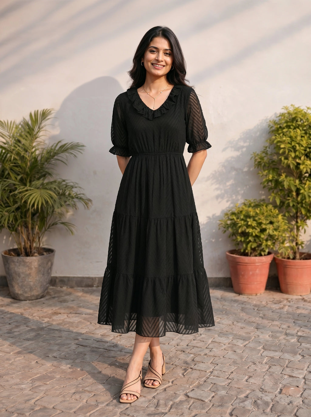 Woman wearing a black dress standing outdoors with plants in the background
