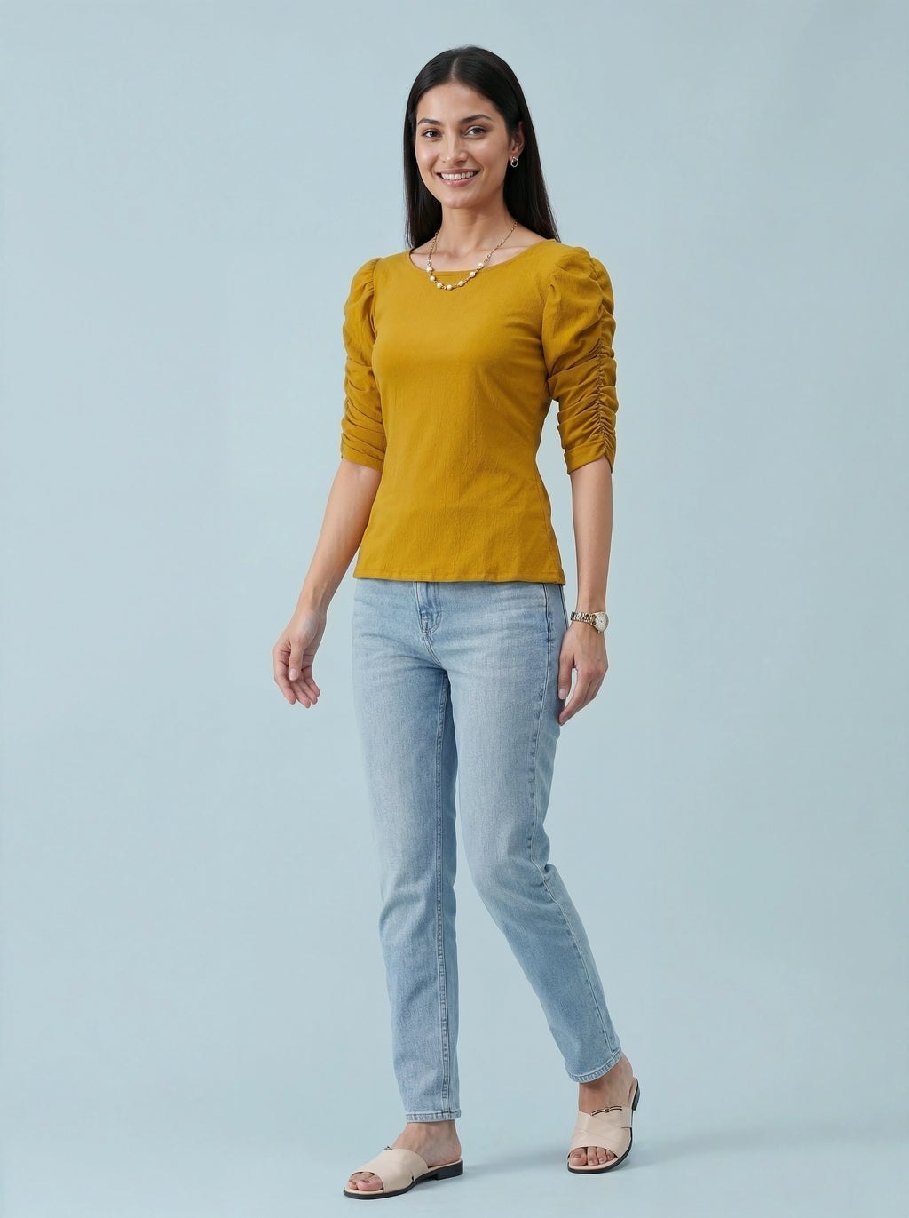Woman wearing a mustard yellow top and light blue jeans on a gray background