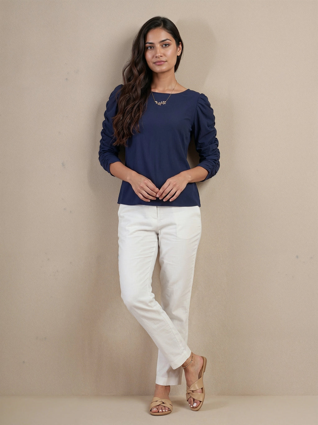 Woman wearing a navy blue top and white pants against a beige background