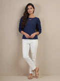 Woman wearing a navy blue top and white pants against a beige background