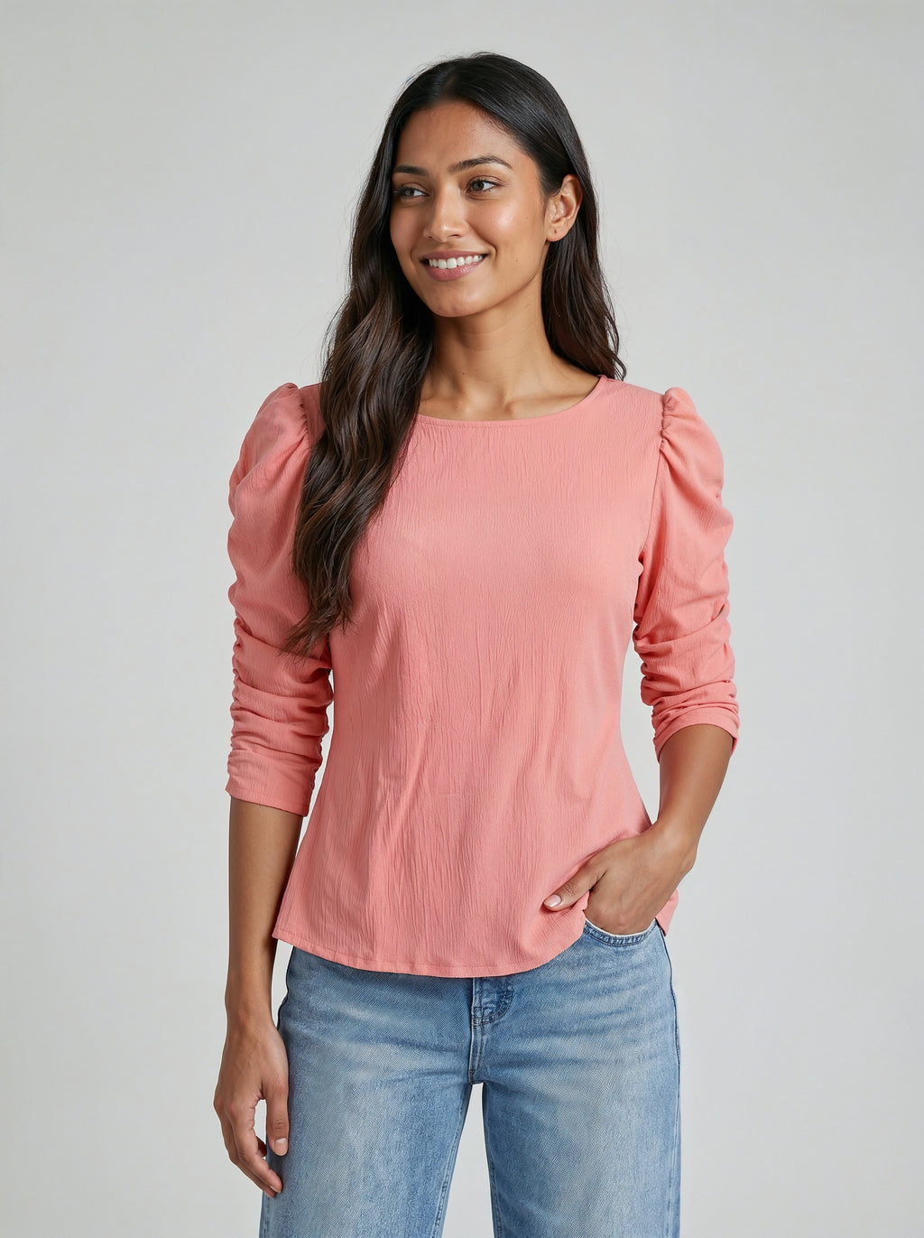 Woman wearing a pink blouse with puffed sleeves and blue jeans on a gray background