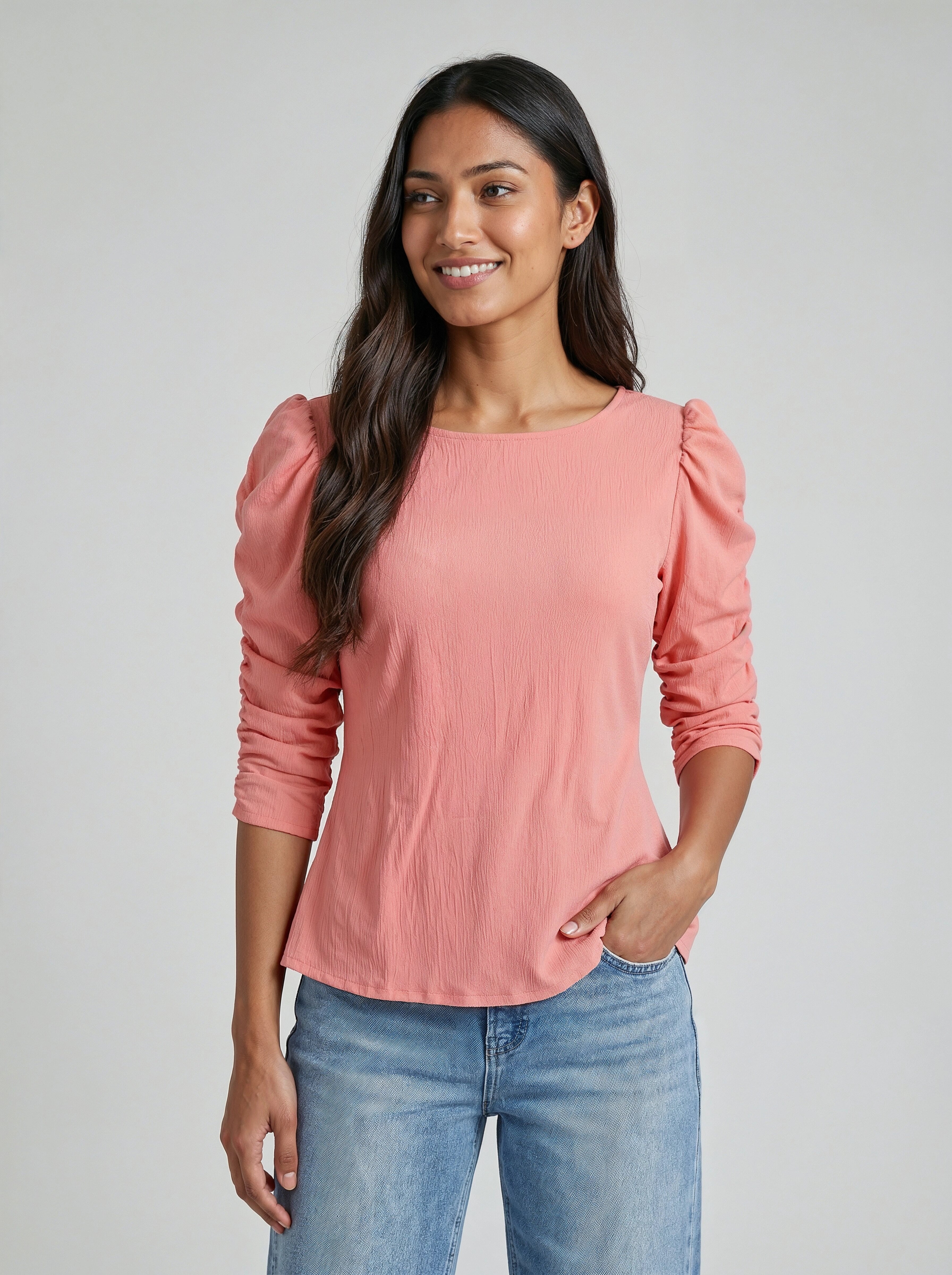 Woman wearing a pink blouse with puffed sleeves and blue jeans on a gray background