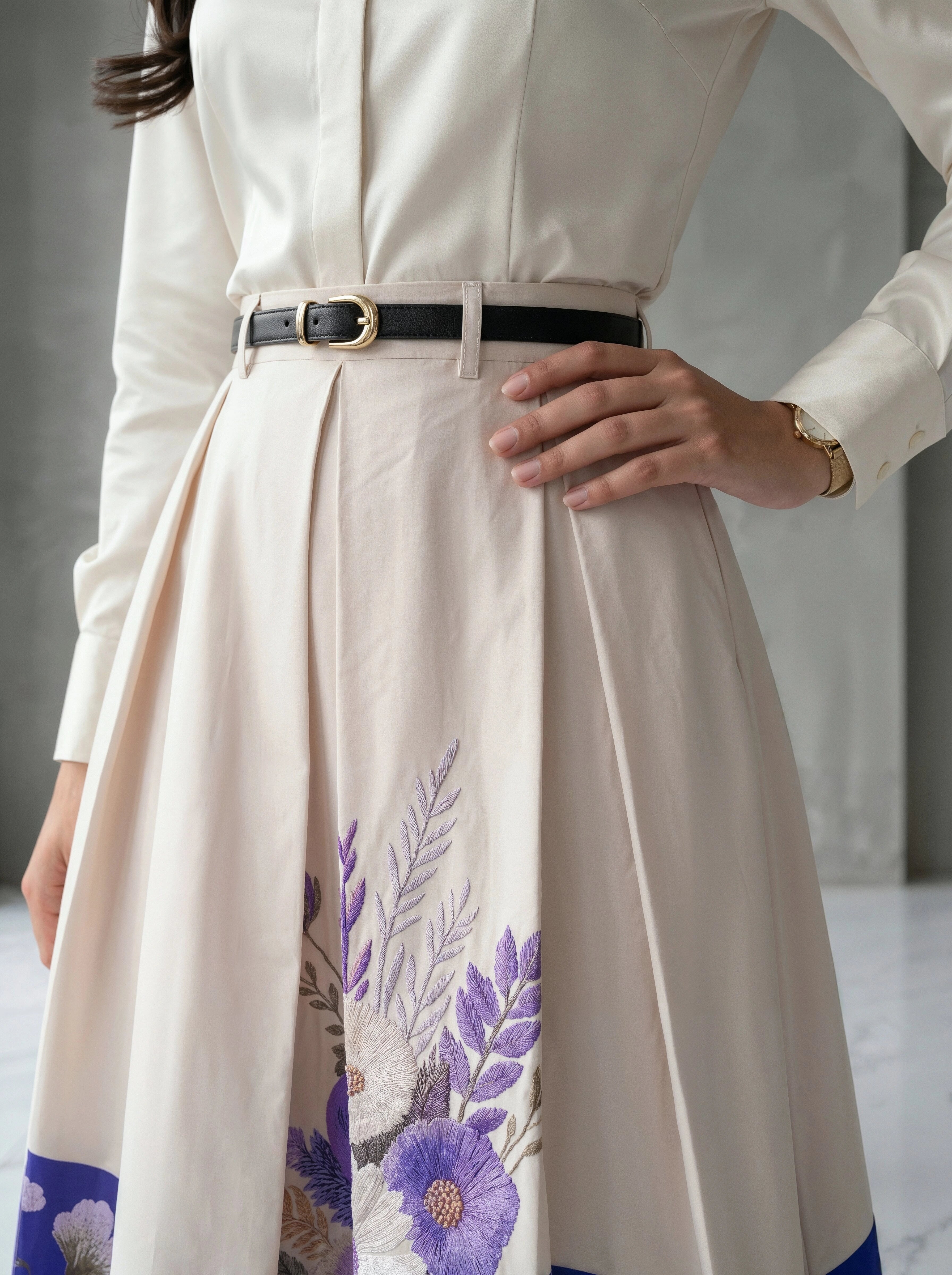 Person wearing a white dress with floral embroidery and a black belt.