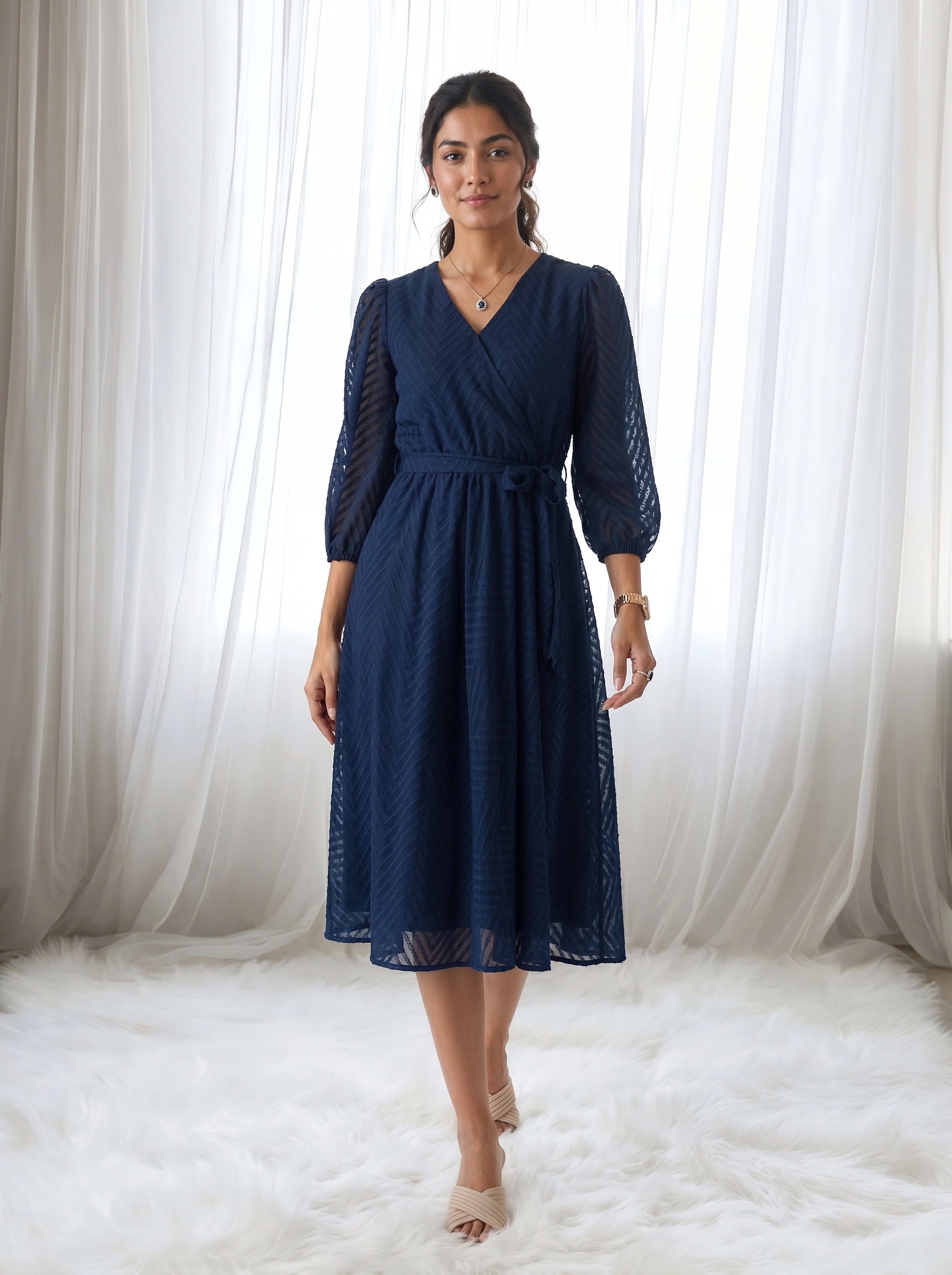 Woman wearing a navy blue dress standing in front of white curtains.