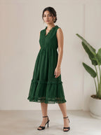 Woman wearing a green dress standing indoors with a plant in the background