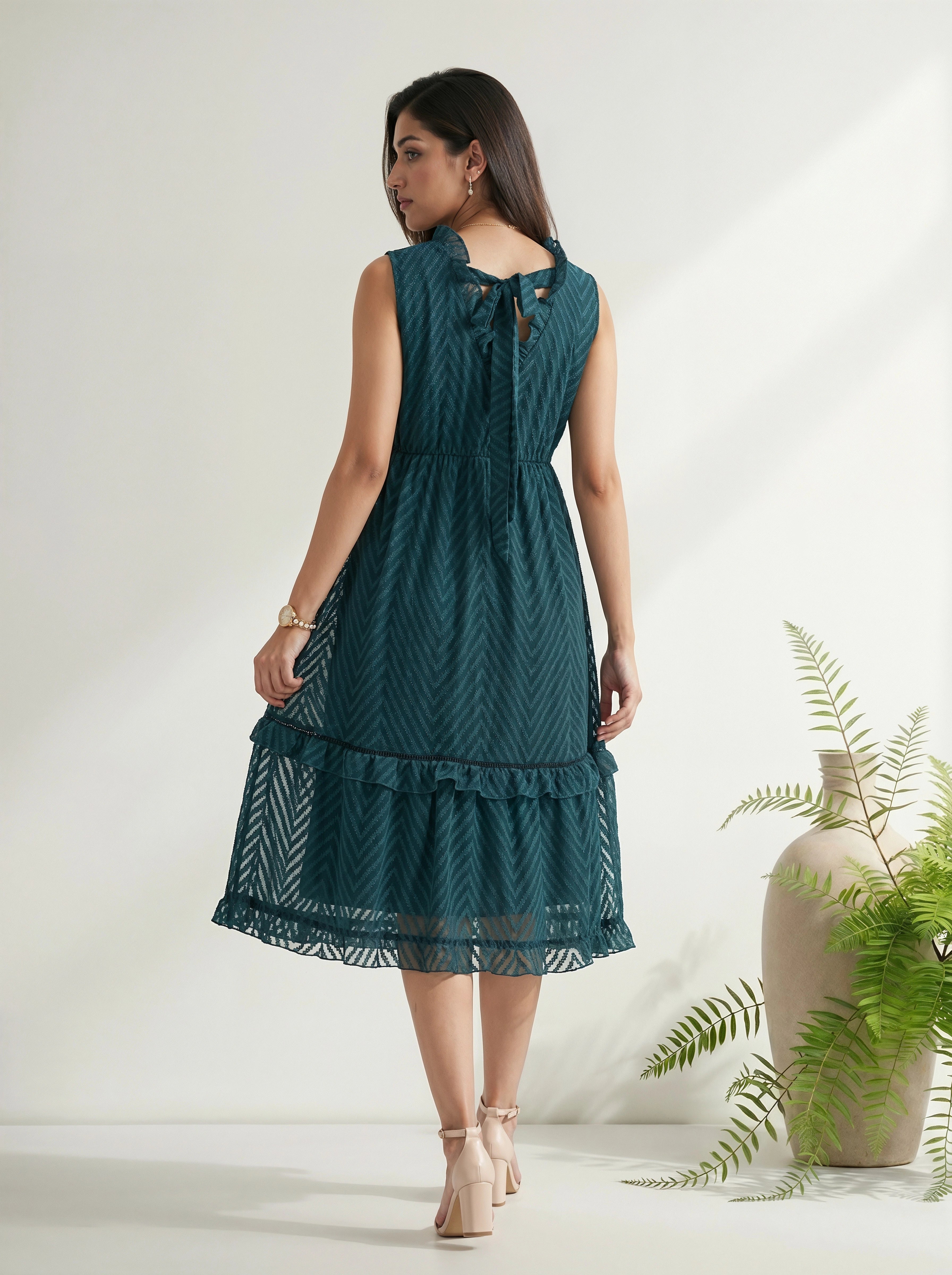 Woman wearing a teal dress with a white background and plant decor