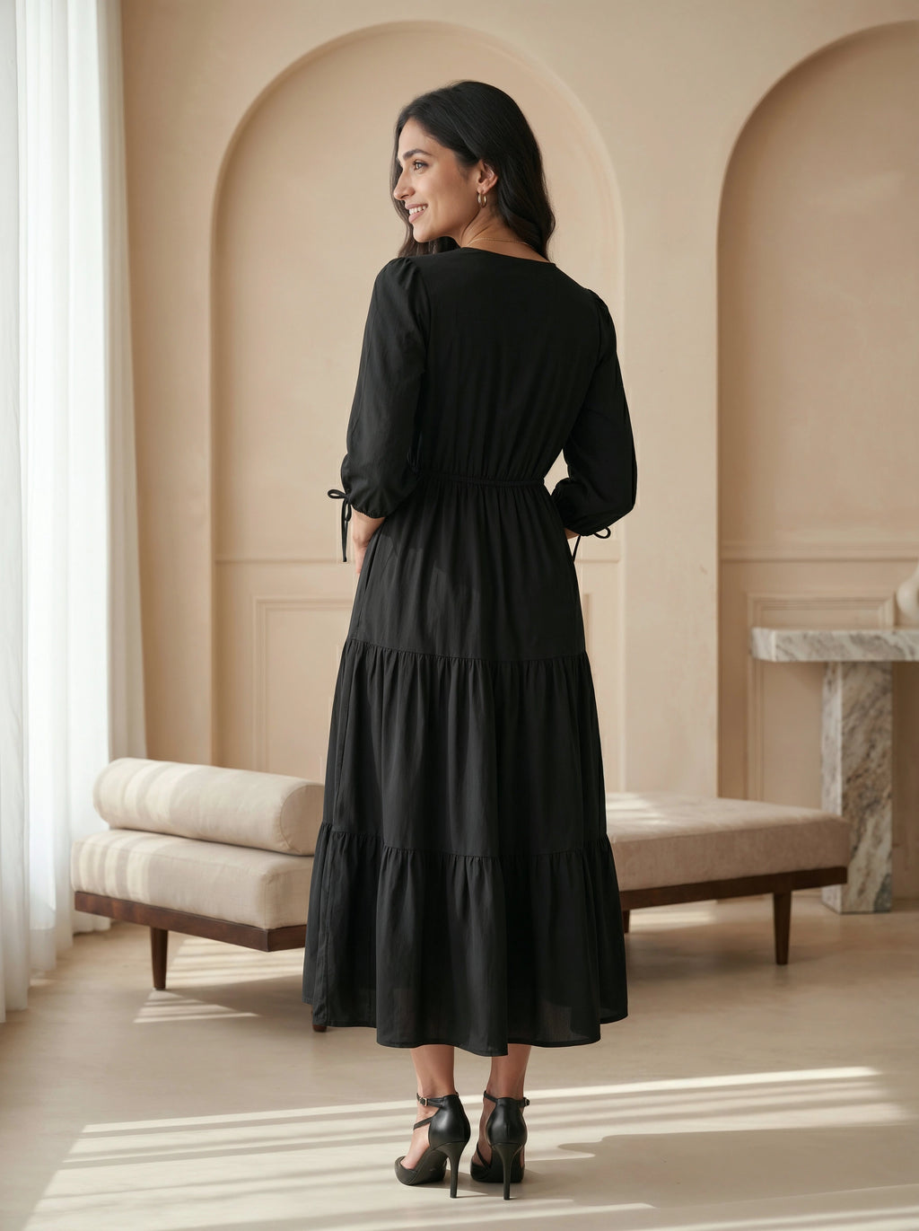 Woman in a black dress standing in a room with beige walls and a bench.