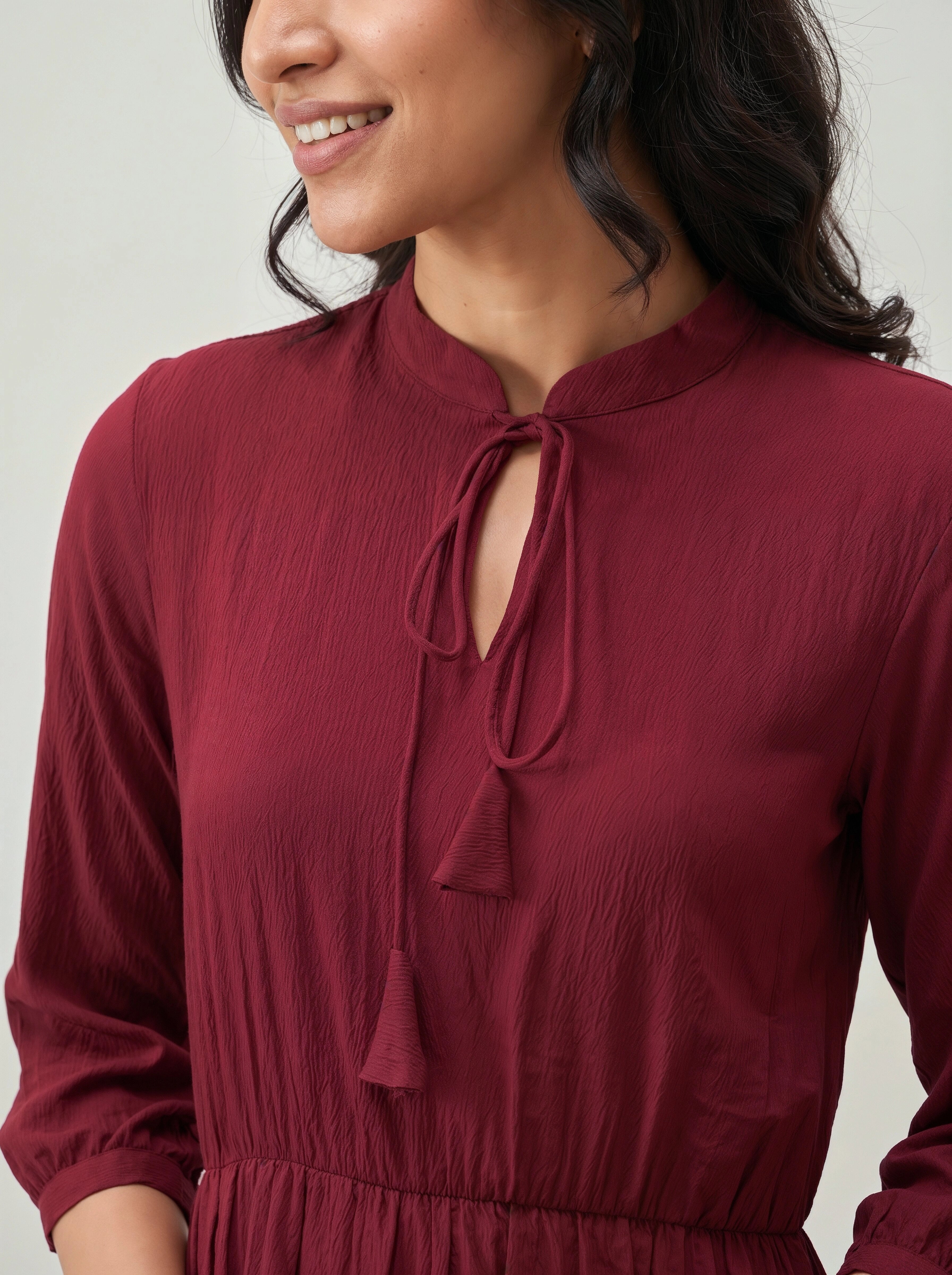 Close-up of a woman wearing a burgundy dress with a tie neckline against a light background